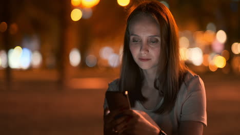 Una-Hermosa-Joven-En-Verano-En-Una-Gran-Ciudad-Nocturna-Mantiene-Un-Teléfono-Inteligente-En-Su-Interior-Y-Escribe-Un-Mensaje-Lee-Correos-Electrónicos-Y-Se-Comunica-En-Salas-De-Chat-Y-Redes-Sociales-Mantiene-Un-Blog-Mira-La-Pantalla-Del-Teléfono